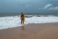 Young woman in yellow rain coat on the beach in heavy rain in Bali