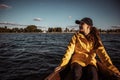 Young woman in yellow raincoat and cap sitting on a boat and looking afield