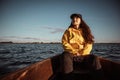 Young woman in yellow raincoat and cap sitting on a boat and looking afield