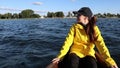 Young woman in yellow raincoat and cap sitting on a boat and looking afield