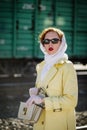 A young woman in a yellow raincoat and dark glasses, with an open handbag in her hands