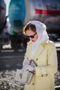 A young woman in a yellow raincoat and dark glasses opens her handbag