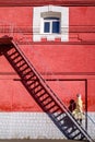 A young woman in a yellow raincoat and dark glasses, with a suitcase in her hands, climbs the fire escape against the background o Royalty Free Stock Photo