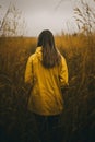 Young woman in yellow raincoat standing in tall grass and looking away Royalty Free Stock Photo