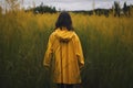 Young woman in yellow raincoat standing in tall grass and looking away Royalty Free Stock Photo