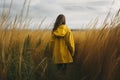 Young woman in yellow raincoat standing in tall grass and looking away Royalty Free Stock Photo