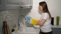 Young woman in yellow rubber gloves in the kitchen is washing dishes by hand. Royalty Free Stock Photo