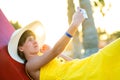 Young woman in yellow summer dress taking selfie with her mobile phone resting on a bench in park Royalty Free Stock Photo