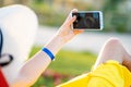 Young woman in yellow summer dress taking selfie with her mobile phone resting on a bench in park Royalty Free Stock Photo