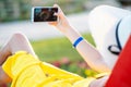 Young woman in yellow summer dress taking selfie with her mobile phone resting on a bench in park Royalty Free Stock Photo