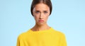 Young woman in yellow sweater is sad and upset on a blue colored background