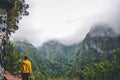 Young woman in yellow sweatshirt on a viewpoint in Levada Caldeirao Verde, Madeira, Portugal. Green scenic mountains in fog, misty