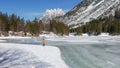 Young woman in yellow winter jacket standing by frozen lake in mountains. Lake Predil, Italy