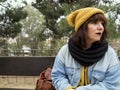 Young woman with yellow woolen cap sitting on a bench worried looking thoughtful