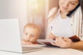 Young woman with baby speaks by phone and working with laptop on kitchen. Business Quarantine Concept Royalty Free Stock Photo