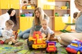 Young women communicate while their kids playing with toys in daycare