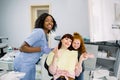 Young woman in dental chair shows thumb up, is ready for dental checkup at modern clinic, her cute little daughter Royalty Free Stock Photo