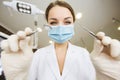 Young women dentist with sterile mask readily approaching a patient with dental instruments held in the hands protected with surgi