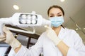 Young women dentist with sterile mask readily approaching a patient with dental instruments held in the hands protected with surgi