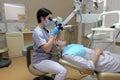 Young woman dentist treating root canals using microscope in the dental clinic. Man patient lying on dentist chair with open mouth Royalty Free Stock Photo