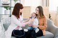 Young woman doctor helping to little baby girl with nebulizer mask, showing how to make inhalation therapy for her