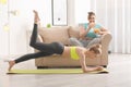 Young woman doing exercise on mat while her stout friend eating chips at home