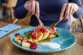 Young women eat breakfast in restaurant. Little pancakes with fruits, fig, raspberry, strawberry, mint and sweet caramel souce