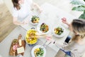 Young women eating dinner together at the table with roasted chicken, potato served with green salad, olives, water