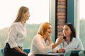 Young women entrepreneurs are discussing a new project while sitting in an office with large windows.