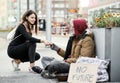 Young woman giving money to homeless beggar man sitting in city. Royalty Free Stock Photo