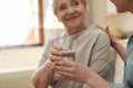 Young woman giving water to elderly lady, focus on hands with glass. Senior people care Royalty Free Stock Photo