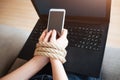 Young woman have social media addiction. Addictivenes from laptop of smartphone. Rope around wrist. Black keyboard. Royalty Free Stock Photo