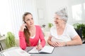 Young woman helping an old senior woman doing paperwork and administrative procedures with laptop computer at home