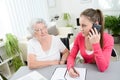 Young woman helping an old senior woman doing paperwork and administrative procedures with laptop computer at home