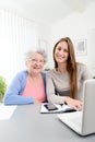 Young woman helping an old senior woman doing paperwork and administrative procedures with laptop computer at home