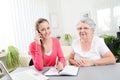 Young woman helping an old senior woman doing paperwork and administrative procedures with laptop computer at home Royalty Free Stock Photo