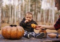 Young woman and her baby son in autumn park, boy playing with helloween pumpkin and eating pumpkin bun. Royalty Free Stock Photo