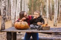 Young woman and her baby son in autumn park, boy playing with helloween pumpkin and eating pumpkin bun. Royalty Free Stock Photo