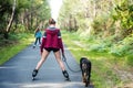 young woman rollerblading with her dog on a cycle path crossing the forest