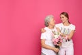 Young woman and her grandmother with flowers on pink background Royalty Free Stock Photo