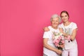 Young woman and her grandmother with flowers on pink background Royalty Free Stock Photo