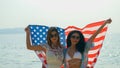 young women hold American flags on the beach and the sea on their summer vacation and they smile and enjoy their vacation Royalty Free Stock Photo