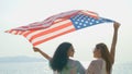 Young women hold American flags on the beach and the sea on their summer vacation and they smile and enjoy their vacation Royalty Free Stock Photo