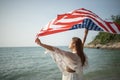 Young women hold American flags on the beach and the sea on their summer vacation and they smile and enjoy their vacation Royalty Free Stock Photo