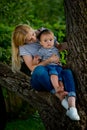 A young woman in jeans and a striped T-shirt and her little daughter are sitting on a tree Royalty Free Stock Photo