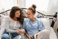 Young women laughing and using cellphones while lying in bed at home Royalty Free Stock Photo