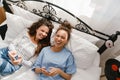 Young women laughing and using cellphones while lying in bed at home Royalty Free Stock Photo