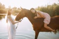 Woman lies astride a horse and other woman stands nearby