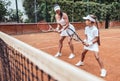 Young woman with llittle girl play tennis standing together by one side on tennis court