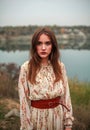 Young woman in long dress and brown boots by lake in countryside in autumn